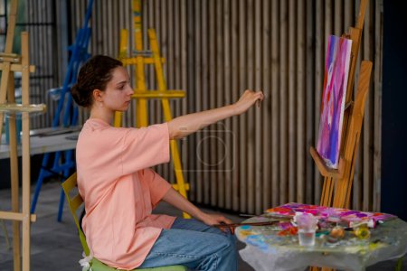Téléchargez les photos : Une fille artiste avec une peau problématique tient un pinceau et mesure les objets en peinture avec le pinceau - en image libre de droit