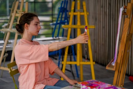 Foto de Una artista con piel problemática sostiene un pincel de pintura y mide objetos en la pintura con el pincel - Imagen libre de derechos