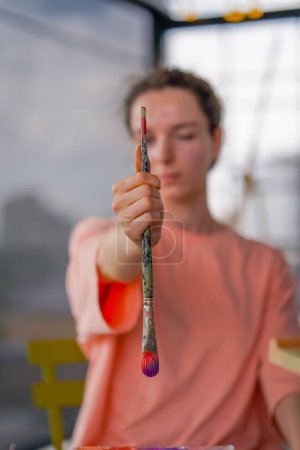 Foto de Una artista con piel problemática sostiene un pincel de pintura y mide objetos en la pintura con el pincel - Imagen libre de derechos