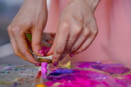 Téléchargez les photos : Gros plan d'une fille artiste pressant de la peinture à partir d'un tube sur une palette de peinture en cours de peinture - en image libre de droit