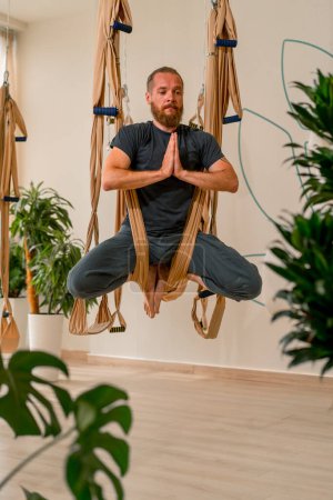 Téléchargez les photos : Athlète masculin adulte s'entraîne et étire le dos sur des feuilles de yoga de mouche dans la salle de gym dans le mode de vie actif de passe-temps aérien - en image libre de droit
