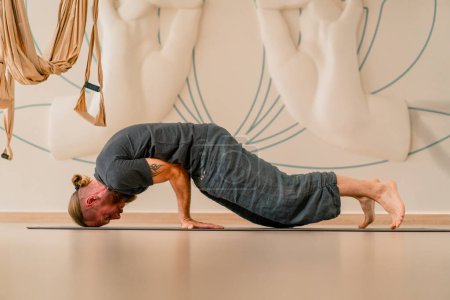 Foto de Un hombre adulto con una barba de yogui hace un handstand de yoga en la hermosa sala de luz hobby estilo de vida activo - Imagen libre de derechos