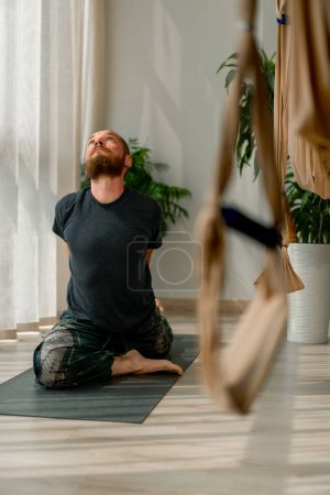 Téléchargez les photos : Homme robuste lève les mains et fait un étirement de tout le corps effectue des éléments de yoga - en image libre de droit