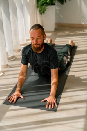 Téléchargez les photos : Homme adulte avec une barbe faisant étirement et dos santé couché sur le sol sport mode de vie actif - en image libre de droit