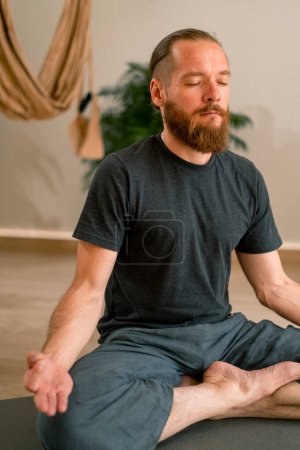 Photo for Adult bearded man in sportswear meditating doing breathing exercises during yoga class in  hall - Royalty Free Image