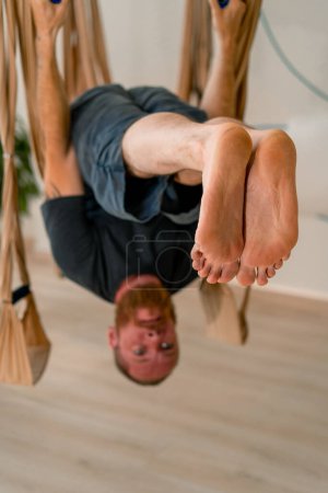 Foto de Un entrenador masculino experimentado cuelga boca abajo en lienzos en un entrenamiento de yoga con mosca en el gimnasio - Imagen libre de derechos