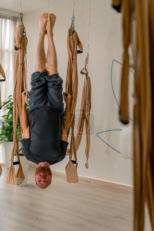 Téléchargez les photos : Un entraîneur masculin expérimenté accroche la tête en bas sur des toiles à un entraînement de yoga de mouche dans la salle de gym - en image libre de droit