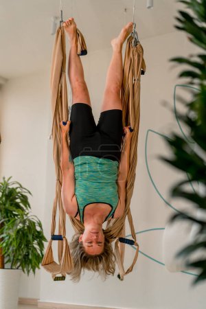 Téléchargez les photos : Une fille en vêtements lumineux pend à l'envers à la formation de yoga de mouche dans le mode de vie actif de passe-temps de gymnase - en image libre de droit
