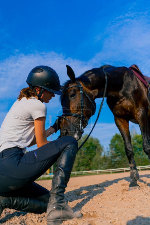 Foto de Una jinete en un casco abraza y rasca su hermoso caballo negro con su mano en la arena ecuestre durante el paseo a caballo - Imagen libre de derechos