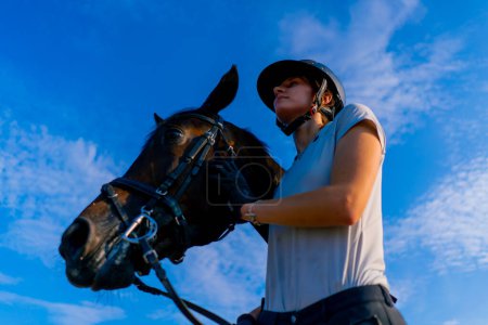 Photo for A helmeted rider leads her beautiful black horse by the harness in the riding arena during horseback ride - Royalty Free Image