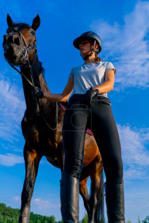 Photo for A helmeted rider leads her beautiful black horse by the harness in the riding arena during horseback ride - Royalty Free Image