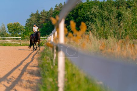Photo for A horsewoman dressed in a helmet rides her beautiful black horse in a horse riding arena during horseback ride - Royalty Free Image