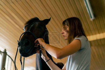 Photo for A rider puts harness on her black horse in the stables in preparation for race equestrian concept - Royalty Free Image