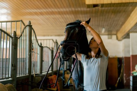 Foto de Un jinete pone arnés en su caballo negro en los establos en preparación para el concepto de carrera ecuestre - Imagen libre de derechos