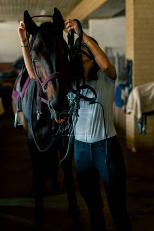 Foto de Un jinete pone arnés en su caballo negro en los establos en preparación para el concepto de carrera ecuestre - Imagen libre de derechos