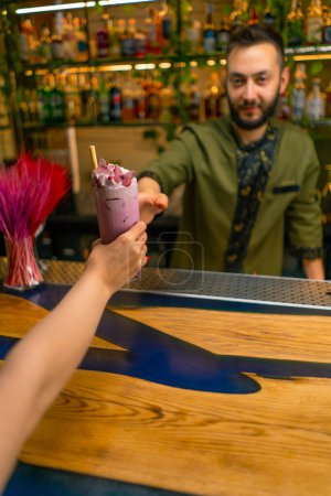 Téléchargez les photos : Mains de barman un cocktail savoureux frais et lumineux à un invité dans un bar ou un restaurant mains rapprochées - en image libre de droit
