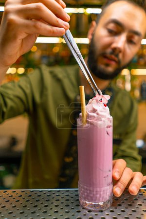 Foto de Un camarero en un bar o restaurante decora un cóctel alcohólico recién preparado presenta decoración con pinzas - Imagen libre de derechos