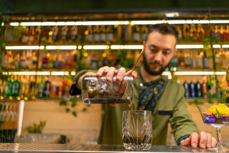 Téléchargez les photos : Le barman expérimenté verse un cocktail alcoolisé savoureux frais de la tasse à mesurer au restaurant du bar en verre - en image libre de droit