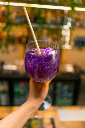 Téléchargez les photos : Gros plan d'une main tenant un cocktail alcoolisé violet fraîchement préparé avec des graines de fruits de la passion dans un bar club fête d'humeur - en image libre de droit