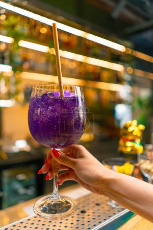 Photo for Close-up of a hand holding a freshly made purple alcoholic cocktail with passion fruit seeds in a bar club festive mood celebration - Royalty Free Image