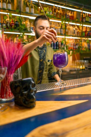 Foto de Un camarero clásico revuelve alcohol en un vaso alto con una cuchara larga para preparar un cóctel en el bar - Imagen libre de derechos
