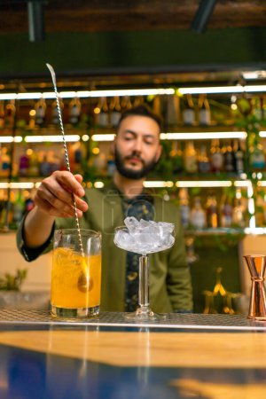 Foto de Un camarero clásico revuelve alcohol en un vaso alto con una cuchara larga para preparar un cóctel en el bar - Imagen libre de derechos