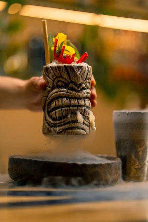 Foto de Mano sostiene un cóctel sabroso alcohólico fresco lo pone en el taburete de la barra donde el nitrógeno líquido se extiende hermosa porción de la bebida en el bar - Imagen libre de derechos