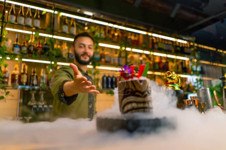 Photo for The bartender shows a fresh alcoholic tasty cocktail that is standing on the bar counter liquid nitrogen spreads spectacular serving at bar - Royalty Free Image