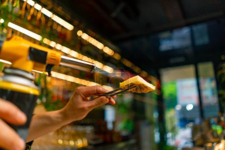 Foto de Un camarero en un bar o restaurante quema un trozo de piña en el fuego para decorar un cóctel alcohólico de cerca - Imagen libre de derechos