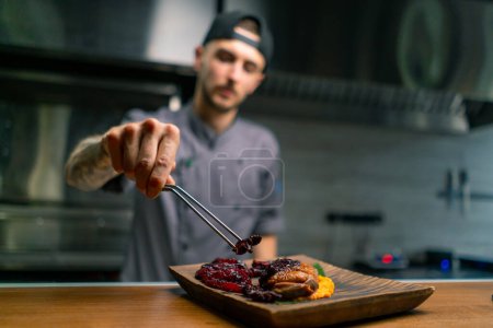 Téléchargez les photos : Cuisine dans un restaurant un chef fixe avec pinces une délicieuse poitrine de canard rôti avec purée de pommes de terre et légumes dans une assiette avec sauce - en image libre de droit