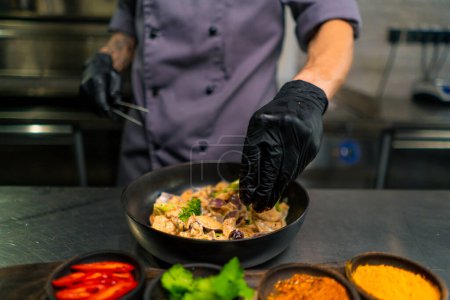 Foto de Primer plano de un chef en una cocina profesional preparando salteado de mariscos mezclando ingredientes en una sartén sosteniendo pulpo bebé con pinzas - Imagen libre de derechos