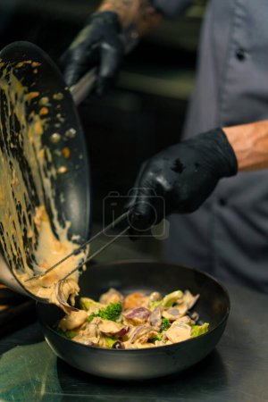Foto de Restaurante chef sirve saute de mariscos deliciosos recién preparados en salsa cremosa en plato cocina asiática profesional - Imagen libre de derechos