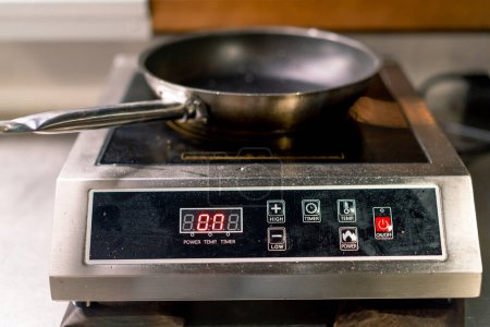 Téléchargez les photos : La cuisinière à induction sur laquelle la poêle est placée est chauffée avant de faire frire la nourriture dans la cuisine professionnelle - en image libre de droit