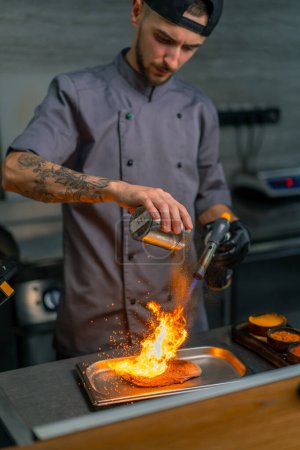 Foto de Primer plano de la mano del chef con quemador de gas freír pechuga de pato crudo en la cocina del restaurante profesional - Imagen libre de derechos