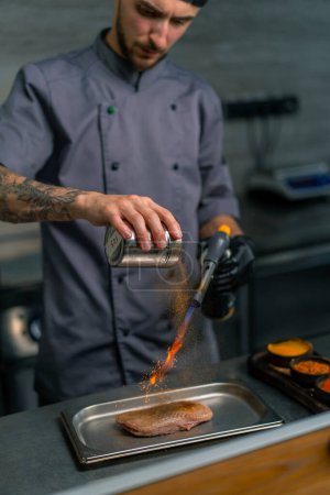 Foto de Primer plano de la mano del chef con quemador de gas freír pechuga de pato crudo en la cocina del restaurante profesional - Imagen libre de derechos