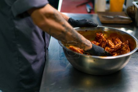 Photo for Professional restaurant kitchen chef stirs chicken wings with spices in bowl asian dish close-up - Royalty Free Image
