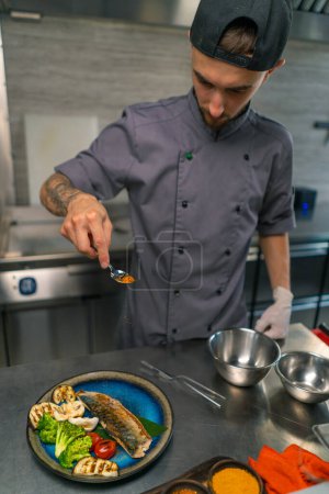 Foto de Restaurante chef sirve pescado dorado recién cocinado y verduras a la parrilla en plato cocina asiática profesional - Imagen libre de derechos