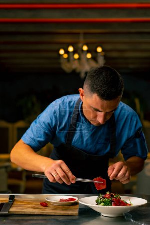 Foto de El chef de un restaurante italiano decora un plato que ha preparado en la cocina profesional - Imagen libre de derechos
