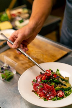 Photo for The chef of an Italian restaurant decorates a dish he has prepared in professional kitchen - Royalty Free Image