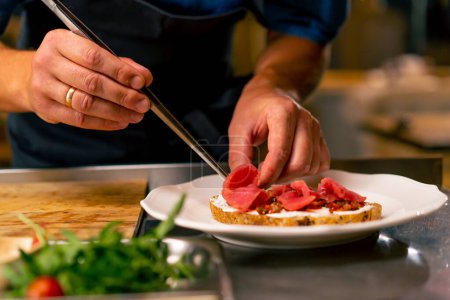 Foto de Un primer plano de un chef preparando bruschetta con aguacate de res y tomates en una cocina profesional en el restaurante italiano - Imagen libre de derechos