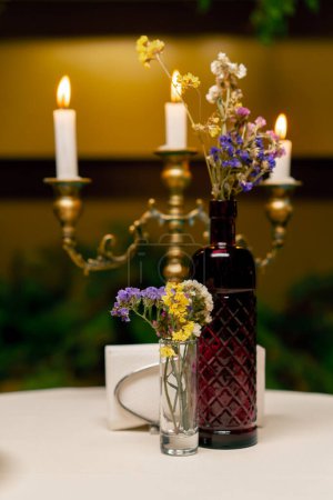 Foto de Primer plano de velas encendidas de pie en un candelero sobre una mesa junto a las flores en el restaurante italiano - Imagen libre de derechos