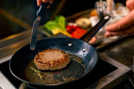 Photo for A close-up of a chef frying a beef patty for a burger in the professional kitchen of Italian restaurant - Royalty Free Image