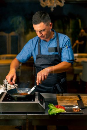 Téléchargez les photos : Gros plan d'un chef avec des pinces dans la main pour faire frire du bacon pour un hamburger dans la cuisine professionnelle du restaurant italien - en image libre de droit