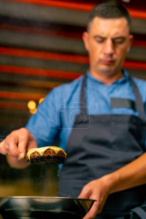 Téléchargez les photos : Gros plan d'un chef tenant une spatule avec laquelle il a enlevé une galette de fromage lors de la cuisson d'un hamburger dans la cuisine du restaurant - en image libre de droit