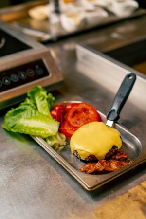Téléchargez les photos : Gros plan d'une escalope de bœuf cuite avec du fromage posé sur une spatule de cuisine à côté des tomates et de la salade dans la cuisine du restaurant italien - en image libre de droit