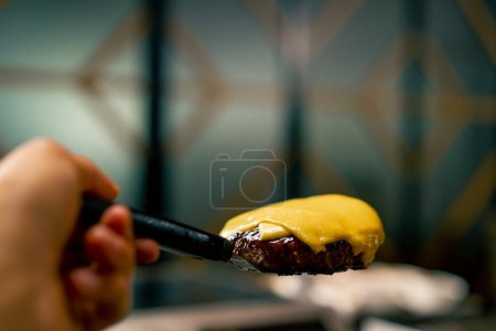 Photo for A close-up of a chef holding a spatula with which he removed a cheese patty while cooking a burger in restaurant kitchen - Royalty Free Image