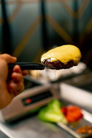 Foto de Un primer plano de un chef sosteniendo una espátula con la que se quitó una empanada de queso mientras cocinaba una hamburguesa en la cocina del restaurante - Imagen libre de derechos