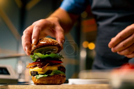Téléchargez les photos : Gros plan d'un chef épinglant un hamburger avec galette de boeuf aux légumes et fromage cuit dans la cuisine professionnelle du restaurant italien - en image libre de droit