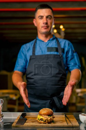 Téléchargez les photos : Le chef du restaurant italien en uniforme montre le hamburger qu'il a cuisiné dans sa cuisine professionnelle - en image libre de droit