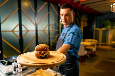Foto de El chef de restaurante italiano en uniforme muestra la hamburguesa que cocinó en su cocina profesional - Imagen libre de derechos